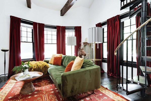 A living room with a green sofa, red curtains, a wooden coffee table, and a staircase.