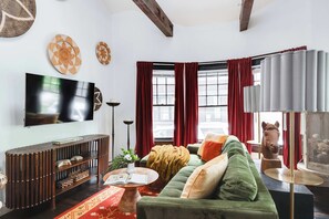 Un salon avec un canapé vert, une console en bois, un téléviseur à écran plat, des rideaux rouges et une sculpture de cheval.