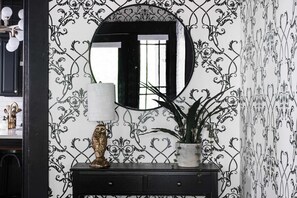 Un mur orné d’un motif noir et blanc, avec un miroir rond placé au-dessus d’une console en bois foncé.