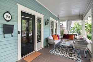 Un porche avec une boîte aux lettres, une plaque portant le numéro « 950 », des meubles en osier et un tapis à motifs.
