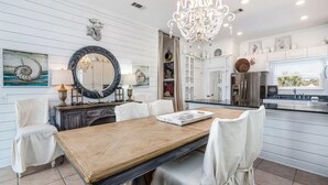 A spacious dining area with a wooden table and white chairs, a large mirror, and a chandelier. - Beachside 8W - 3BD Gulf-Front Townhome, 2 Decks, Sleeps 10 (Panama City Beach)