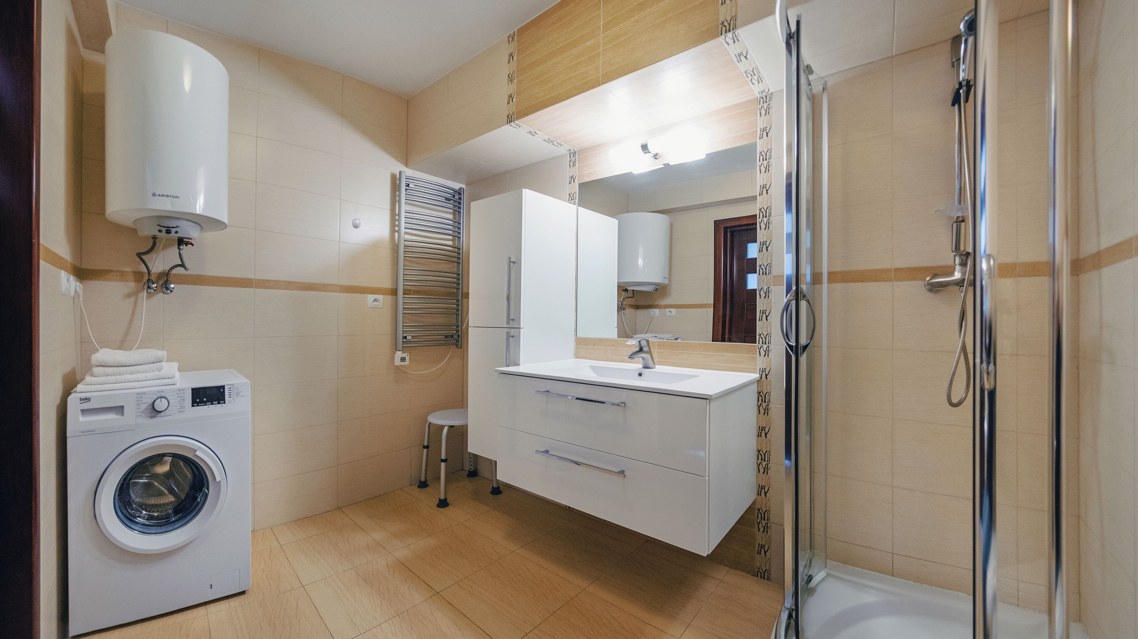Une salle de bain moderne équipée d’un lave-linge, d’un évier, d’un miroir et d’une douche.
