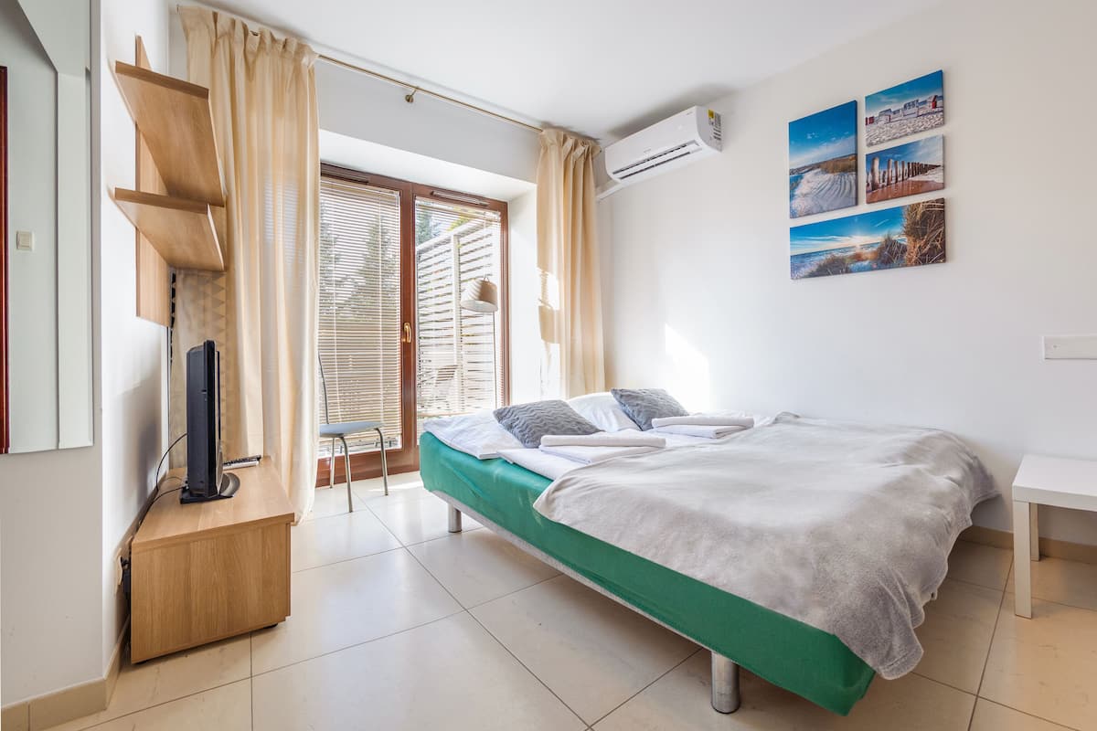 Ein Schlafzimmer mit Bett, Schreibtisch, Stuhl, Klimaanlage und einem Fenster mit Jalousien.