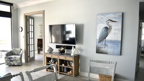 A living room with a television, a painting of a bird, a wooden cabinet, and a bench. - One of a Kind Penthouse--All New! A Beach Lover's Dream Vacation Rental+Locker!! (Myrtle Beach)