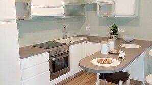 Una cocina moderna con armarios blancos, un horno de acero inoxidable, un fregadero y una pequeña isla con taburetes.