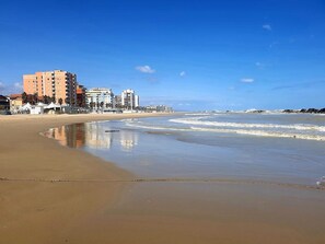 Une plage avec un rivage sablonneux, un ciel bleu dégagé et des bâtiments en arrière-plan.