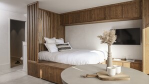 Quarto moderno com cama, painéis de madeira, uma mesa redonda com chávenas e uma televisão.