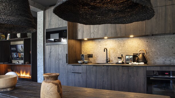 A modern kitchen with dark wood cabinets, a stainless steel microwave, a coffee maker, and a kettle on the counter. - Apartment FERRONNE by JAPANDI home (Megève)
