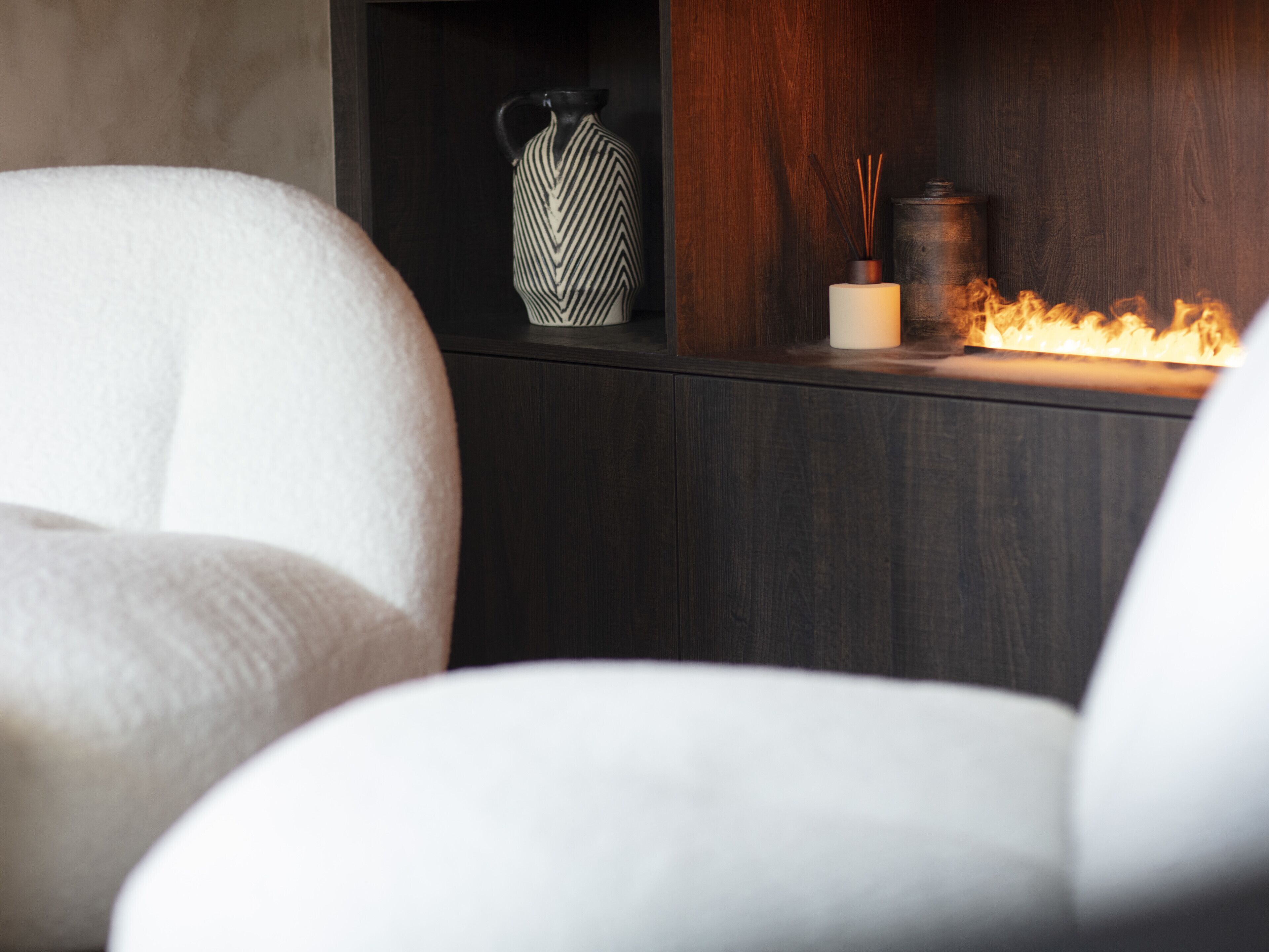 A modern interior with a dark wooden cabinet, a white vase, and a candle holder with a lit candle.