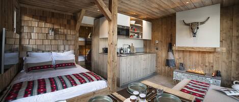 Un interior de madera con una cama, una mesa de comedor para dos, una zona de cocina y una decoración de cabeza de toro montada en la pared.