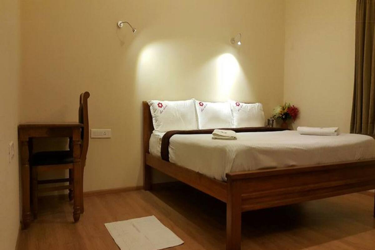 A bedroom with a wooden bed, white bedding, a wooden chair, and a nightstand with a vase.