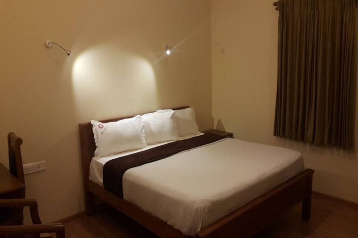A neatly made bed with white linens and a dark headboard in a room with beige walls and a wooden floor.