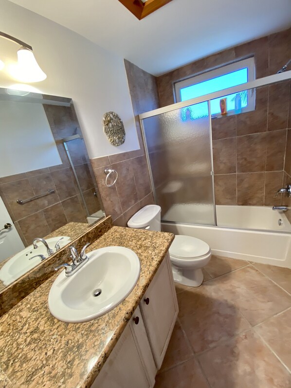 Een badkamer met een granieten aanrecht, een witte wastafel, een toilet en een bad.