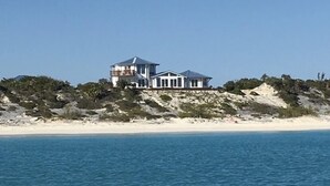 A large, multi-story beachfront property with a prominent balcony and a clear view of the ocean.