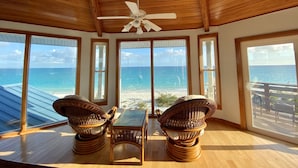 A room with a wooden ceiling, large windows, wicker furniture, and a ceiling fan.