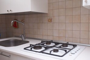 A kitchen with a stainless steel sink, a gas stove with four burners, and a red towel hanging on the faucet.