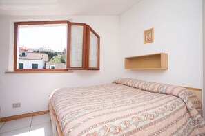 A bedroom with a bed, a window, a picture frame, and a wooden shelf.