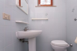 Une salle de bain avec un lavabo blanc, des toilettes, un miroir et une fenêtre ornée d’un cadre décoratif.