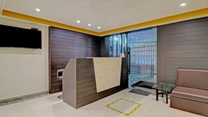 Ein modernes Hotelzimmer mit Empfangstresen, einer Glastür, die nach draußen führt, einer kleinen Sitzecke und einem großen Fenster.