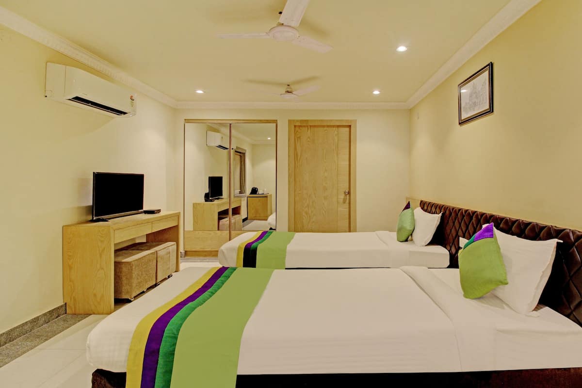 A hotel room with two beds, a TV, a desk, and a mirror.