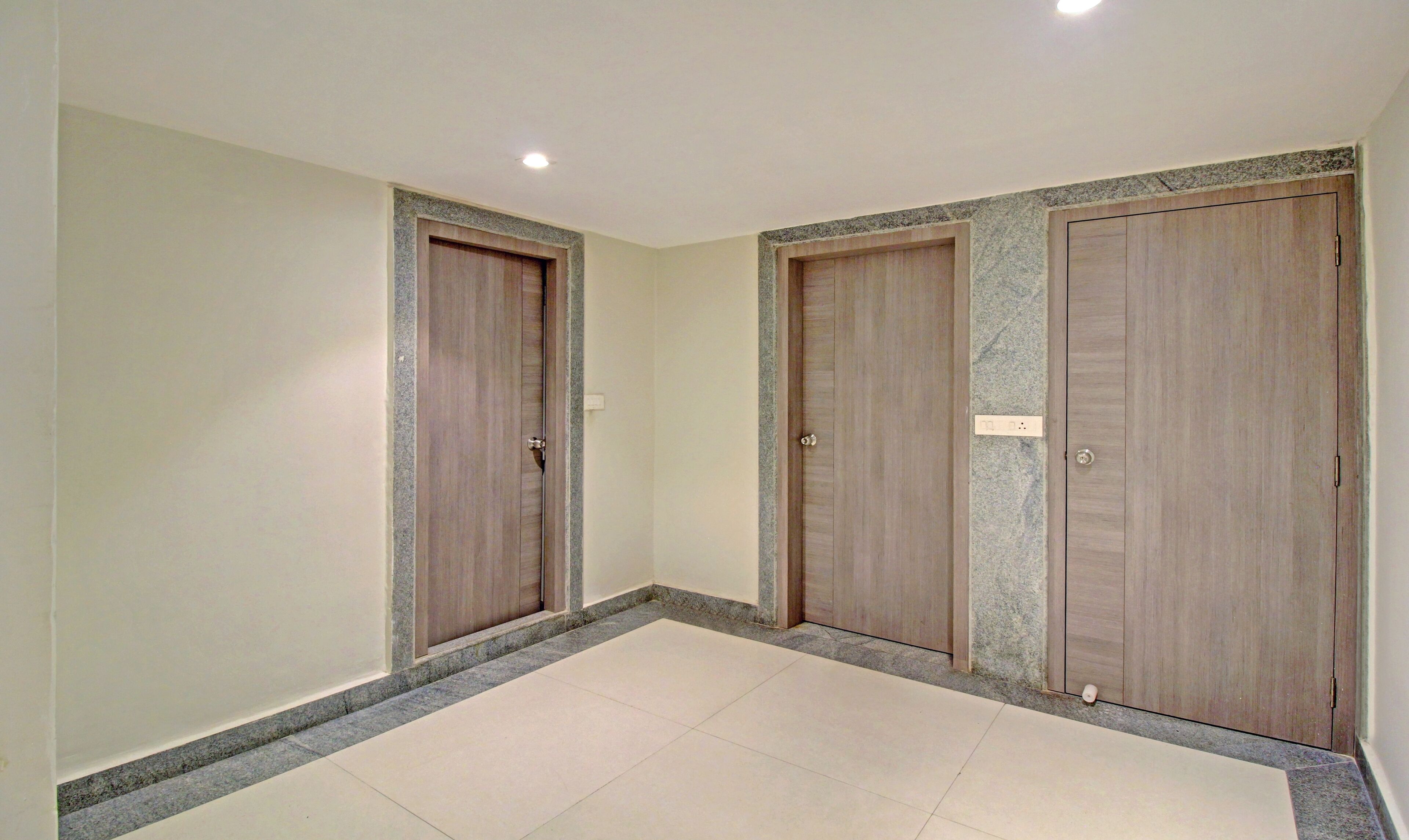 A hallway with three wooden doors, each with a marble-like border, and a tiled floor.