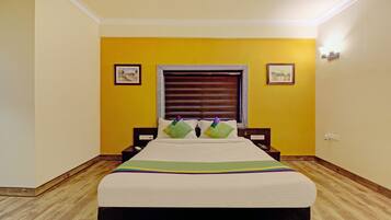 Quarto com uma cama, janela com persianas, duas fotos emolduradas nas paredes e piso de madeira.