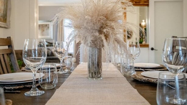 Une table à manger dressée avec de la vaisselle transparente et un vase contenant des herbes de la pampa séchées.