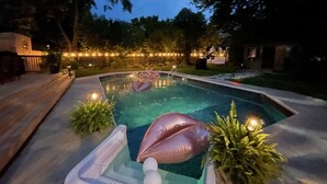 Une piscine extérieure avec des jeux gonflables, entourée d’une terrasse en bois et agrémentée de plantes en pot.