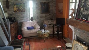 A living room with a stone wall, a sofa, a coffee table, a fireplace, and a painting. - Maison D'artiste Atypique (Saint-Hippolyte-du-Fort)