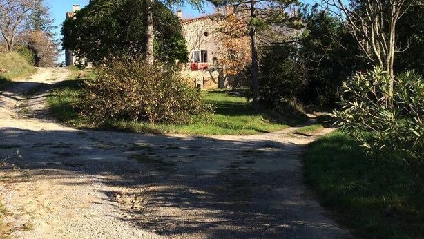 A rural road leading to a stone building with a red roof, surrounded by trees and shrubs. - Maison D'artiste Atypique (Saint-Hippolyte-du-Fort)