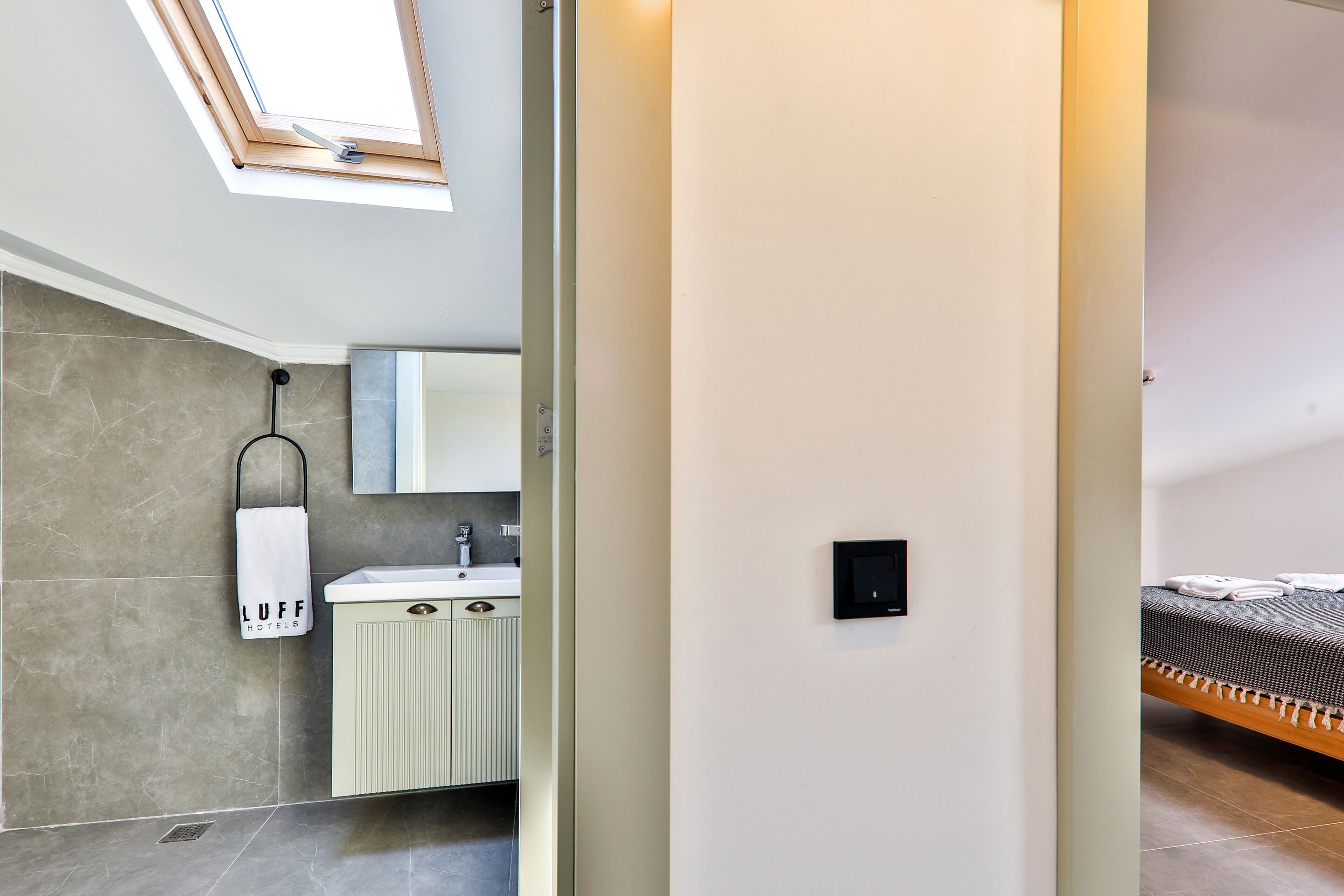 A modern hotel room with a skylight, a bathroom with a towel rack, and a neatly made bed.