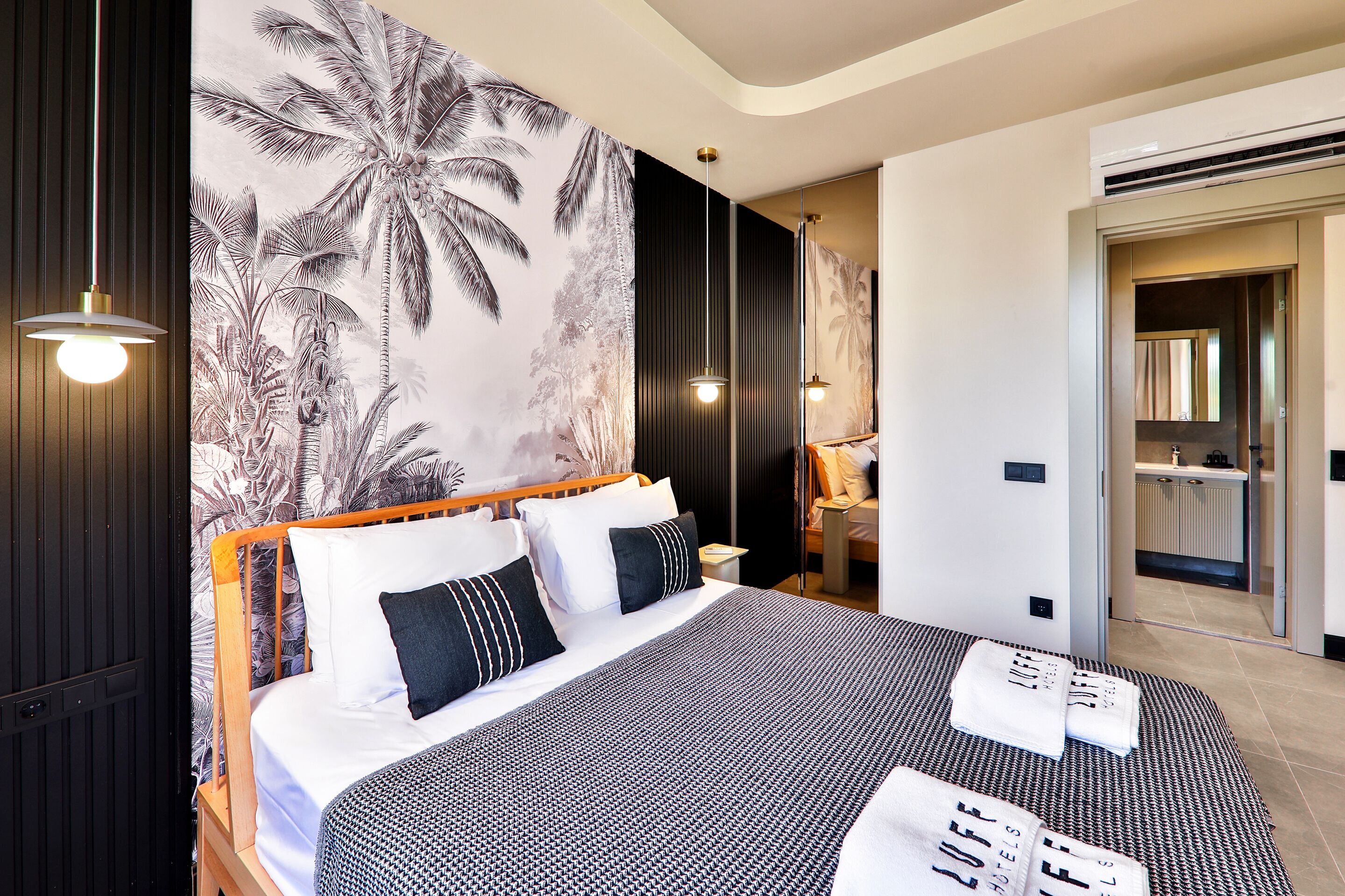 Ein modernes Hotelzimmer mit einem großen Bett, tropischem Wandpapier und einem durchgegangenen Tür sichtbaren Badezimmer.