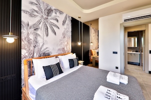 A modern hotel room with a large bed, a tropical wallpaper, and a bathroom visible through an open door.