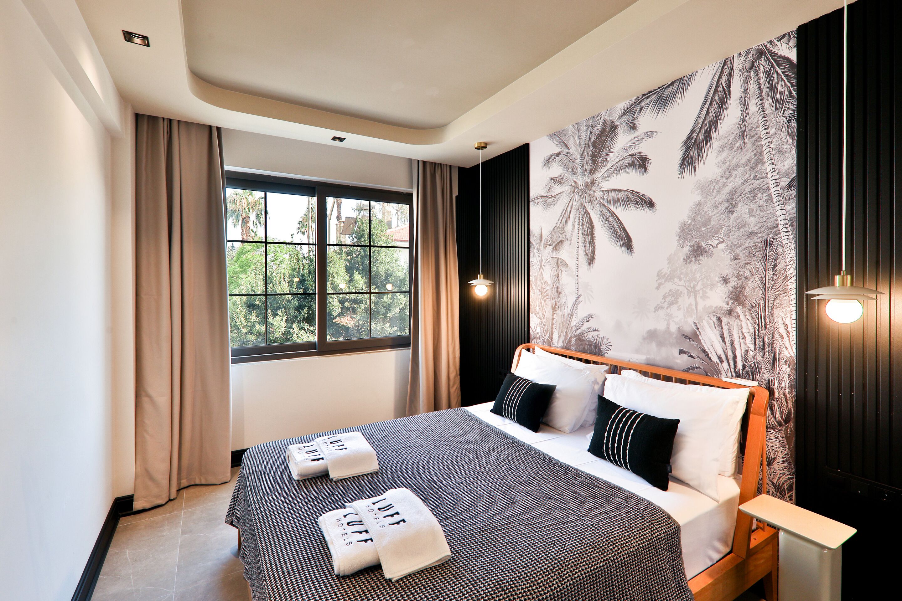 Habitación de hotel moderna con una cama grande, vista a zonas verdes a través de la ventana y un mural tropical en la pared.