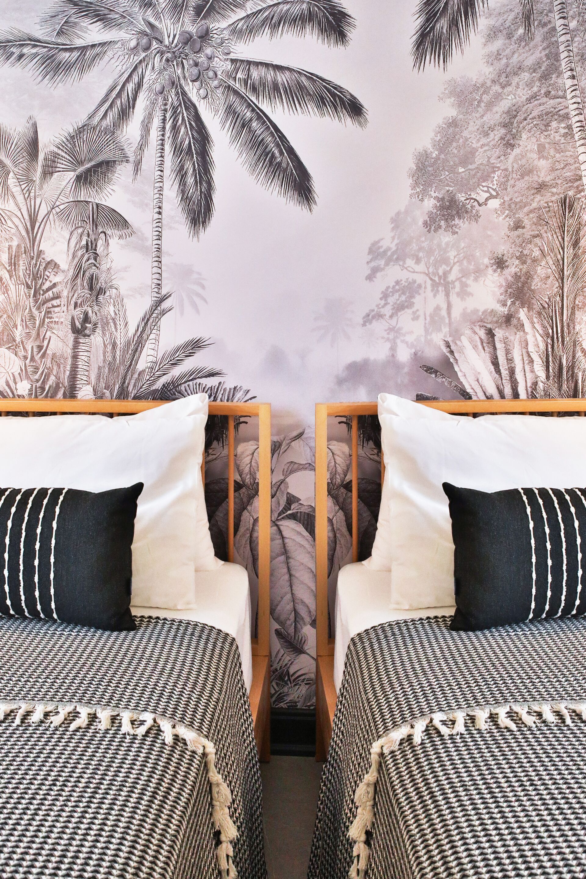 Habitación con dos camas, cada una con cabecera y almohadas, y un mural de palmeras en la pared.