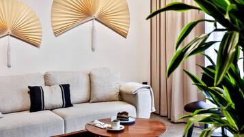 A modern living room with a sofa, two wall-mounted fans, a coffee table with a cake, and a potted plant.