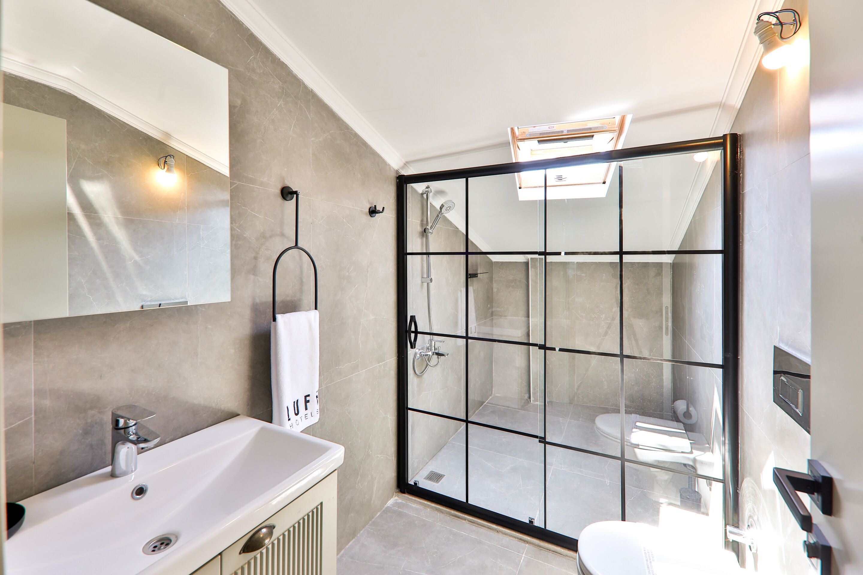 A modern bathroom with a glass-enclosed shower, a white sink, and a towel hanging on the wall.