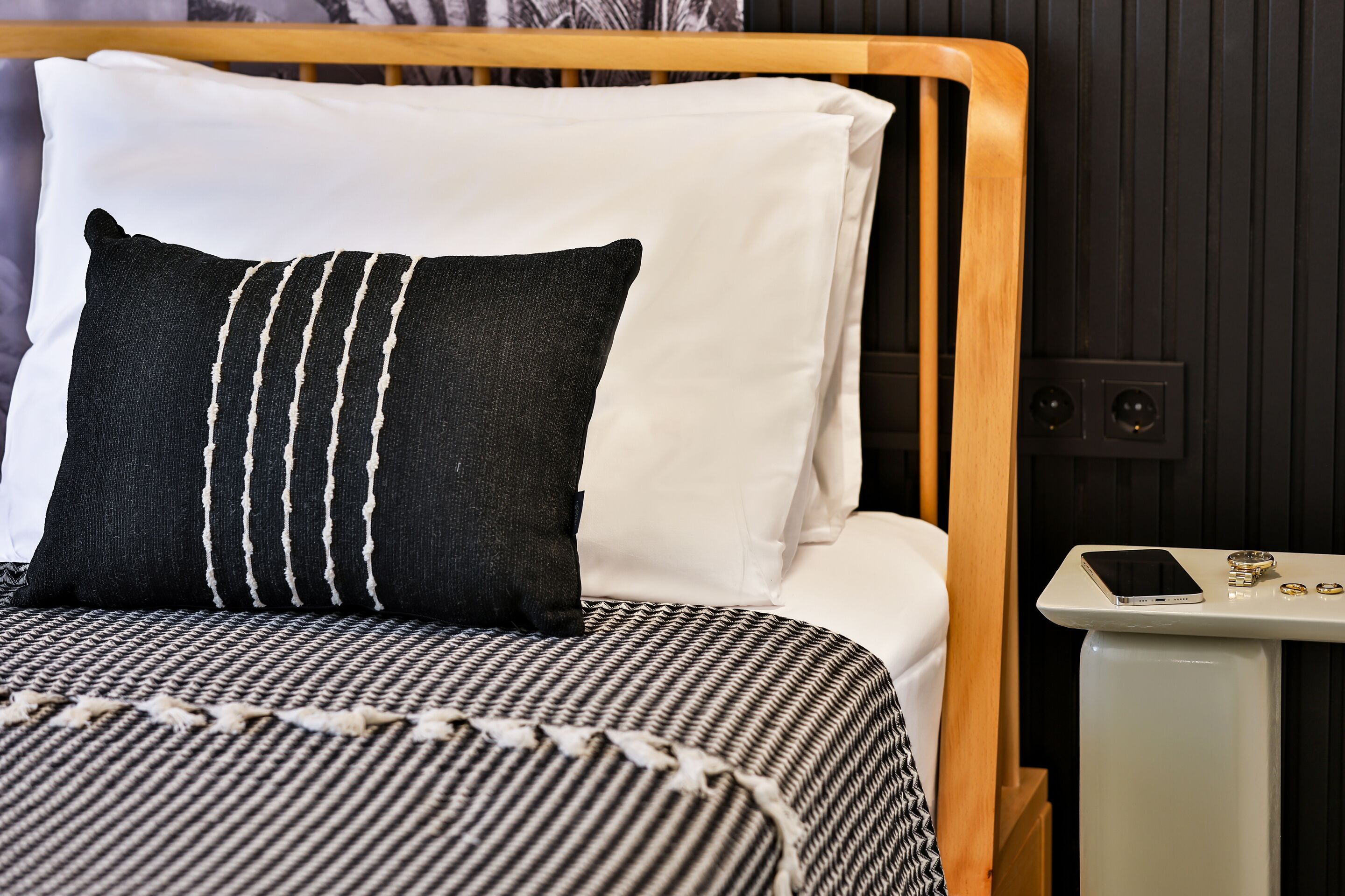 Una cama con una colcha a rayas, un almohadón blanco y uno negro.