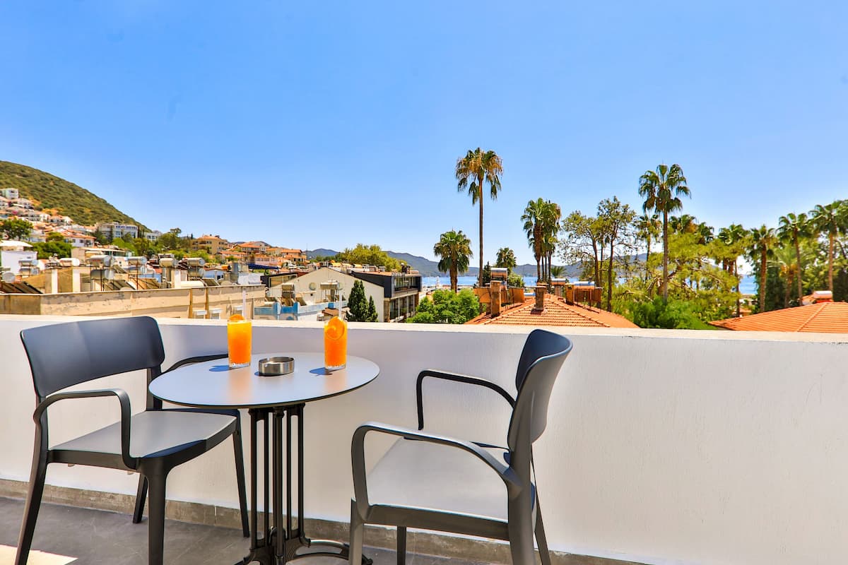 Una terraza con dos sillas y una mesa, con vistas a un pueblo costero con edificios y palmeras.