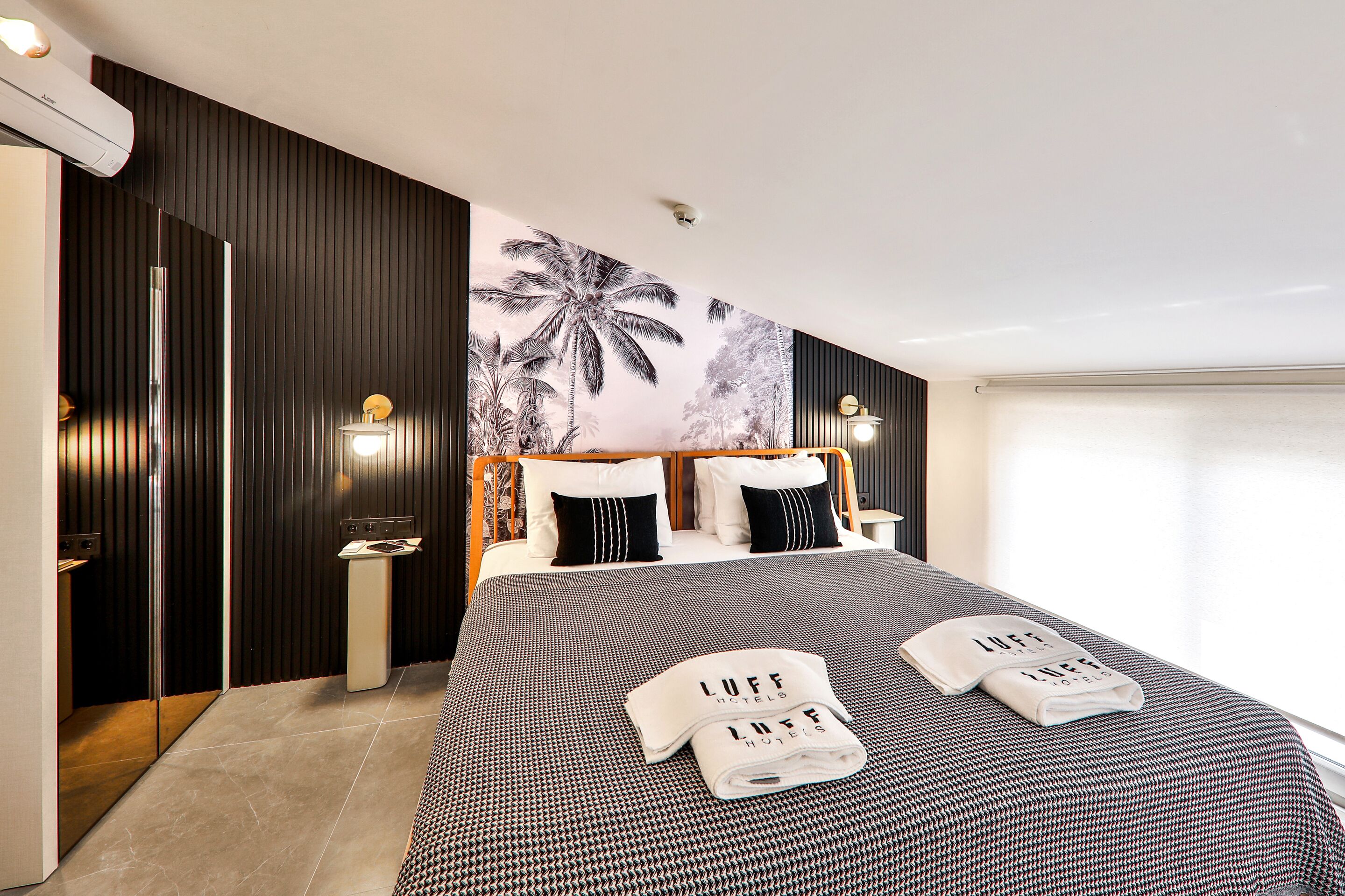 A modern hotel room with a large bed, a wall mural, and a bathroom with a mirror and sink.