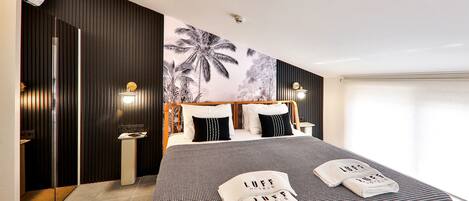A modern hotel room with a large bed, a wall mural, and a bathroom with a mirror and sink.