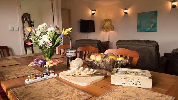 A dining table set with food, a vase of flowers, and a tea sign. - Superb new cottage, stunning views, secluded but handy to Hahndorf Main Street (Hahndorf)