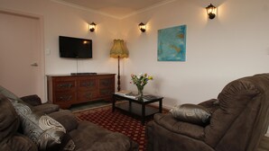 A living room with brown leather sofas, a flat-screen TV, a wooden cabinet, a table with a vase of flowers, and wall-mounted lights. - Superb new cottage, stunning views, secluded but handy to Hahndorf Main Street (Hahndorf)