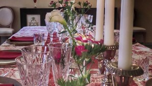 Een eettafel gedekt met kristal glazen, witte kaarsen en een bloemstuk.
