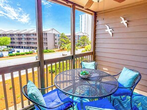 A balcony with a round table, chairs, and a view of buildings and a road.