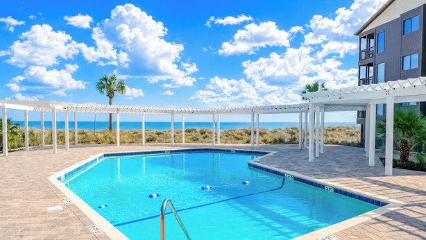A swimming pool with clear blue water, surrounded by a white pergola and a building with large windows. - Stay at Tilghman Beach & Racquet Club 241 a second-row 3BR condo just steps from the sand with two balconies, pools, and tennis courts. (North Myrtle Beach)