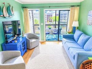 A living room with a TV, sofa, chairs, a table, and a balcony with a view.