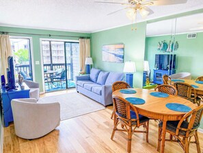 A living room with a sofa, a dining table with chairs, a television, and a ceiling fan. - Tilghman Beach & Racquet Club 241 (North Myrtle Beach)