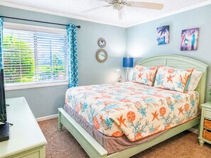 A bedroom with a bed, a desk, a ceiling fan, and a window with curtains.