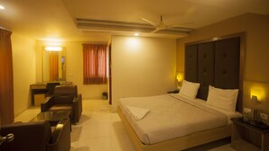 A hotel room with a bed, a desk, a chair, and a ceiling fan. - Ganesh Meridian (Tiruppattur)